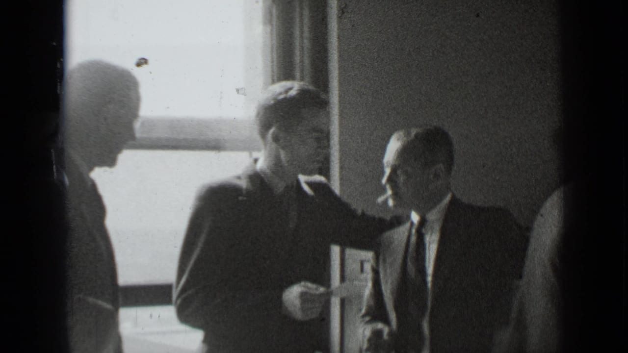 Three men in suits stand near a bright window in a dim interior.