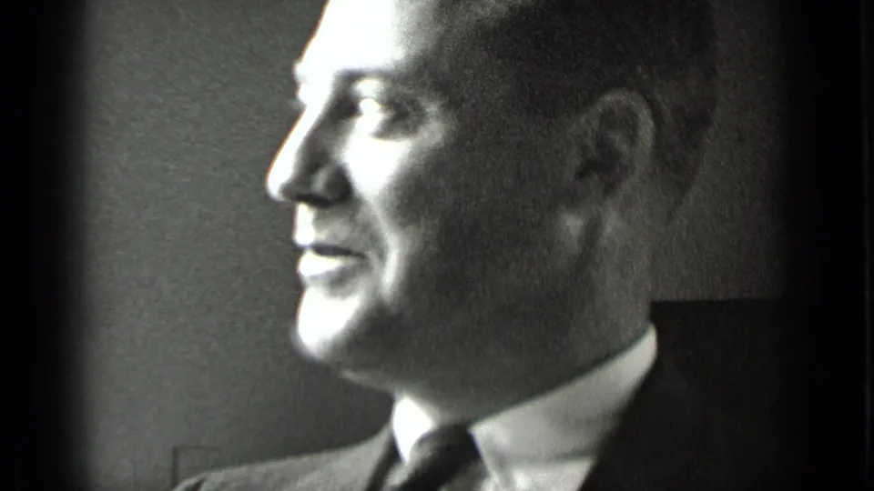 Close-up of a suited man in profile, softly lit in black-and-white 8mm footage from the 1939 New York clip.