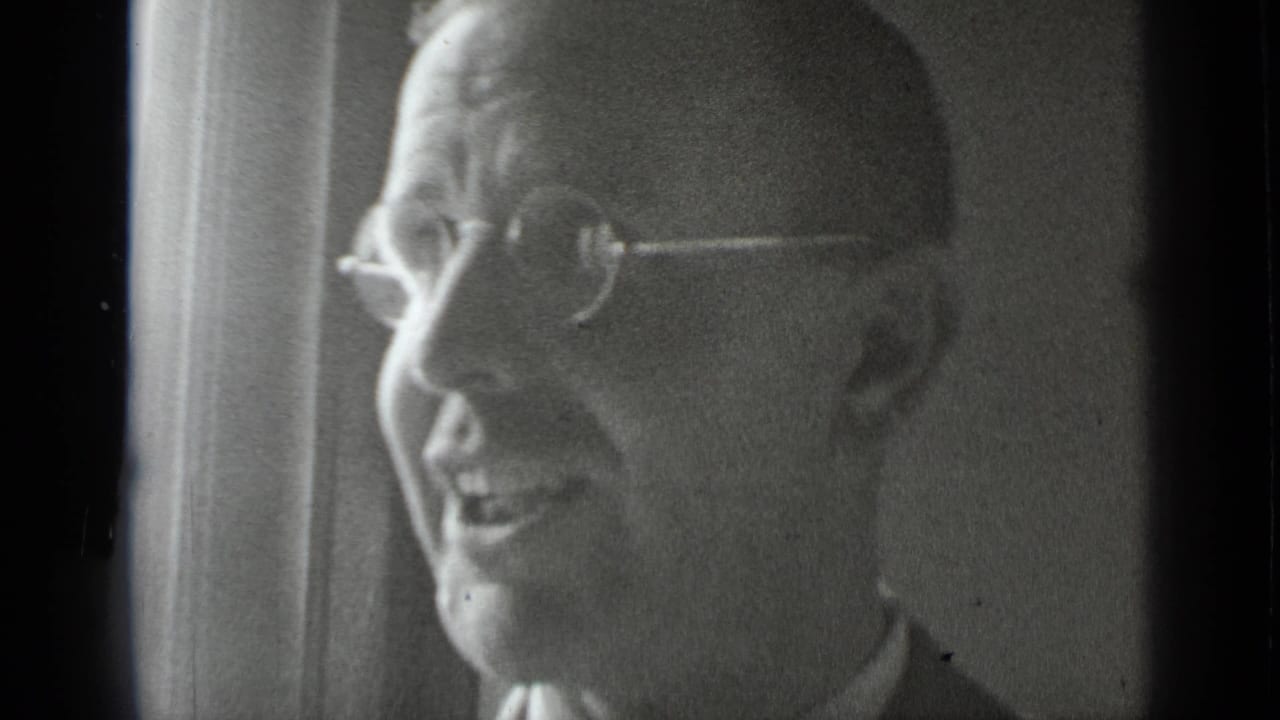 Older man in round glasses smiling or speaking in profile.