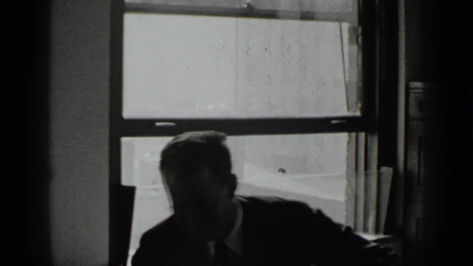 The man shifts to one side near the end of the 8mm clip, still silhouetted against the large window.