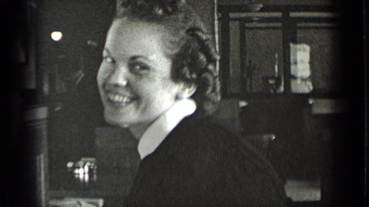 In supported 1939 New York footage, a woman in a dark dress with a white collar smiles near a workplace sink.