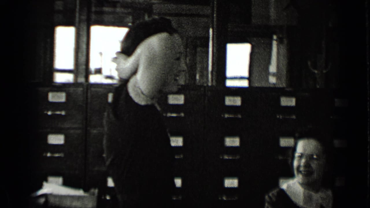 Two women are in a filing room with rows of cabinets behind them.