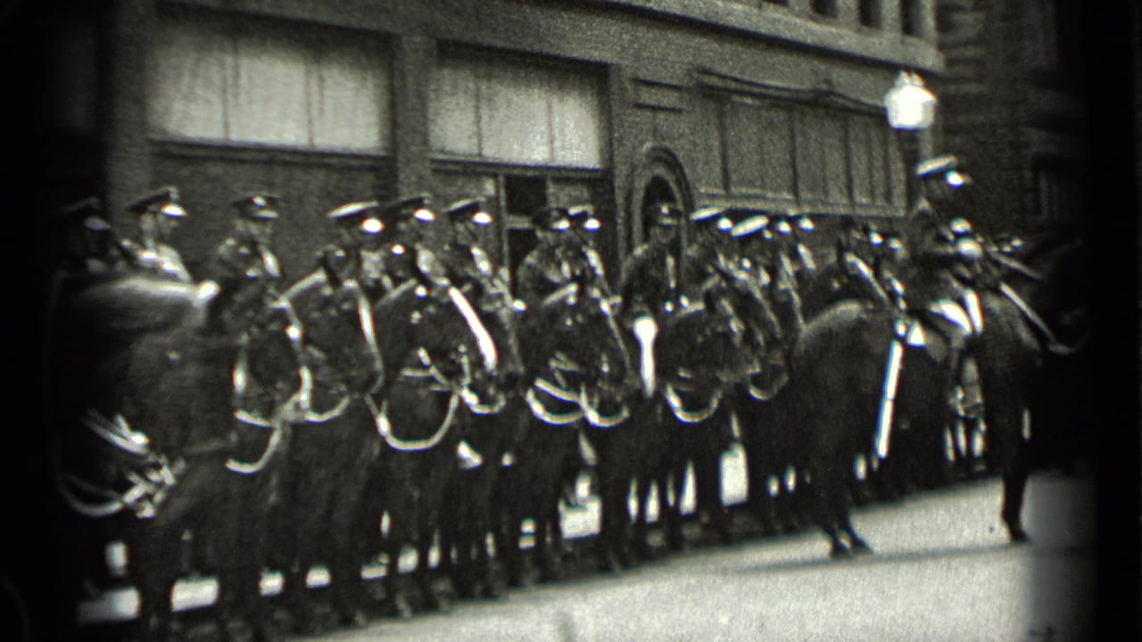 Mounted uniformed officers line up with horses beside a city building.