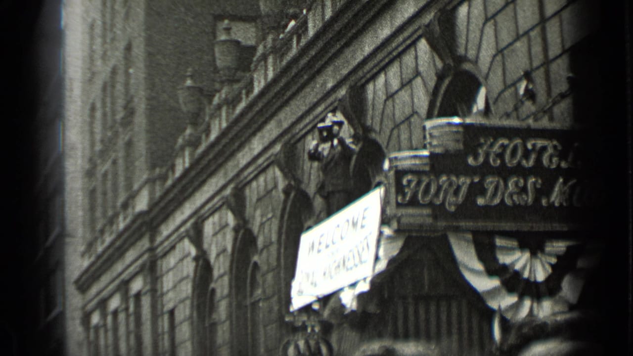 Hotel facade with hanging sign, welcome placard, and a person holding a camera near the entrance.