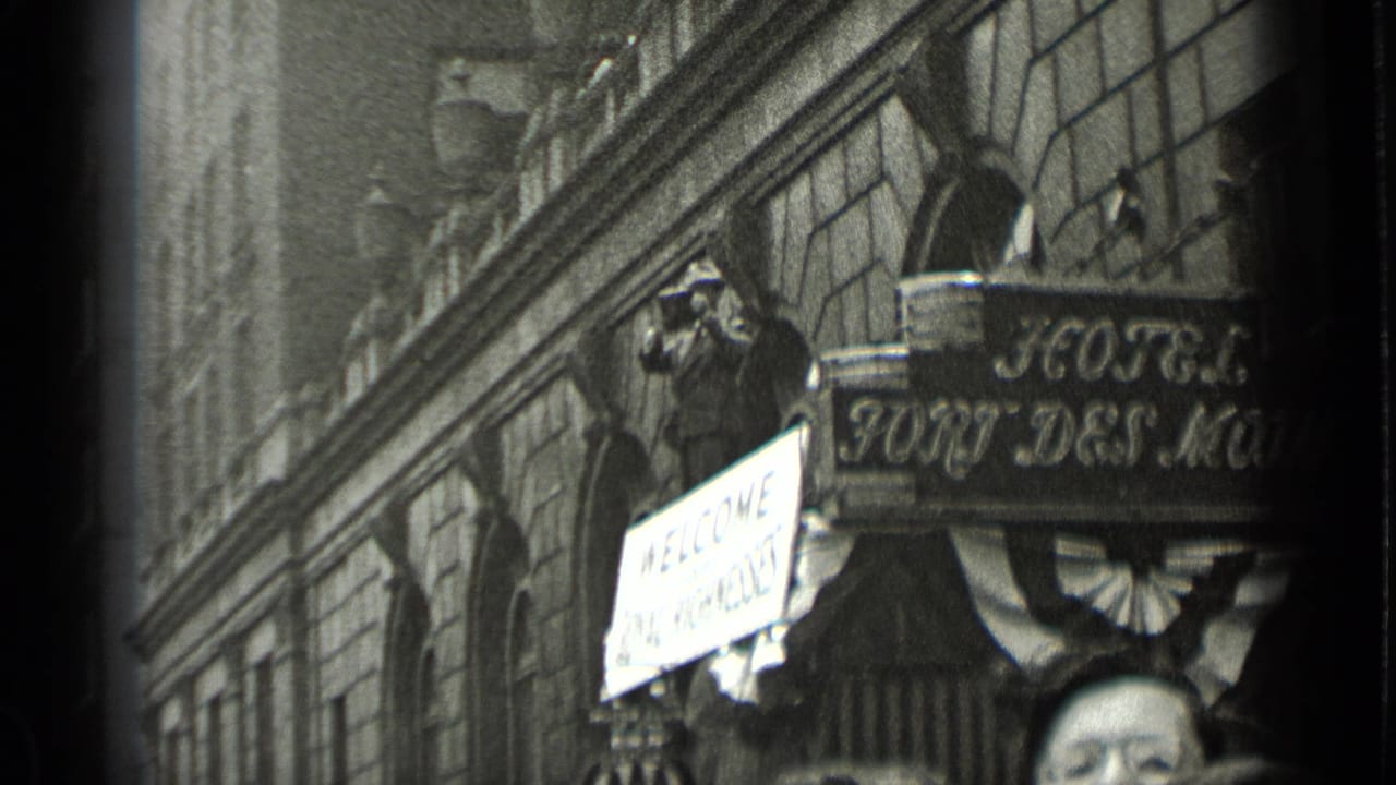 Hotel sign and welcome placard above a crowd, with a photographer standing near the facade.
