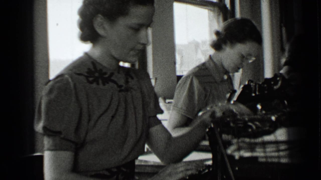 Two women seated at office desks with manual typewriters near bright windows.