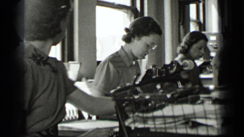 Women continue office typing and paperwork in the 1939 New York interior, with foreground figures partly blocking the view.