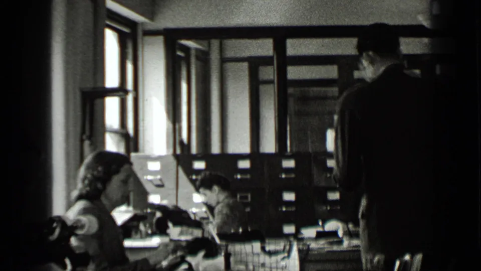 In the 1939 New York office footage, a man stands near women working at desks with typewriters and filing cabinets nearby.