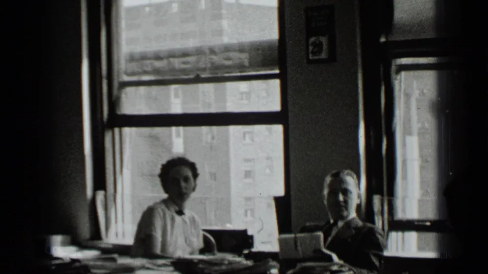 1939 New York office interior with women seated near tall windows, papers on desks, and buildings visible outside.