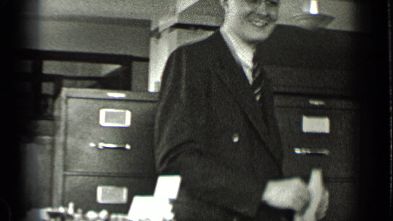 Smiling man in a suit standing near filing cabinets in an office.