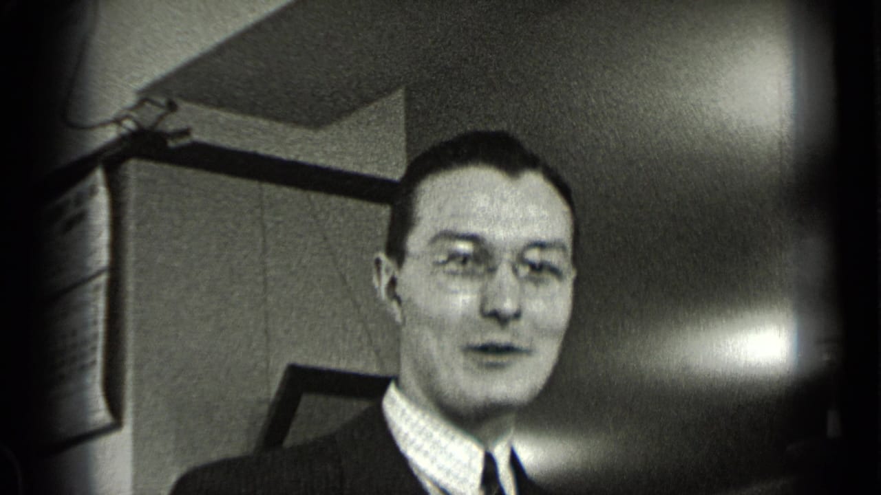 Man wearing glasses and a suit speaking inside an office.