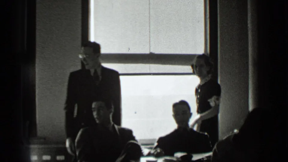 A wider 1939 New York office view shows several adults gathered near a large window, with some seated and others standing.