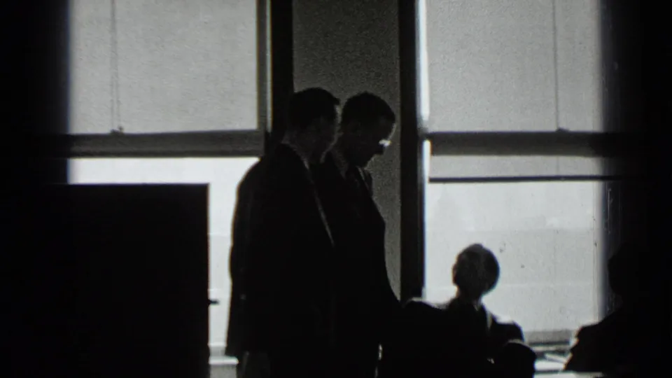 In a 1939 New York interior, silhouetted suited adults appear to confer near large backlit windows.