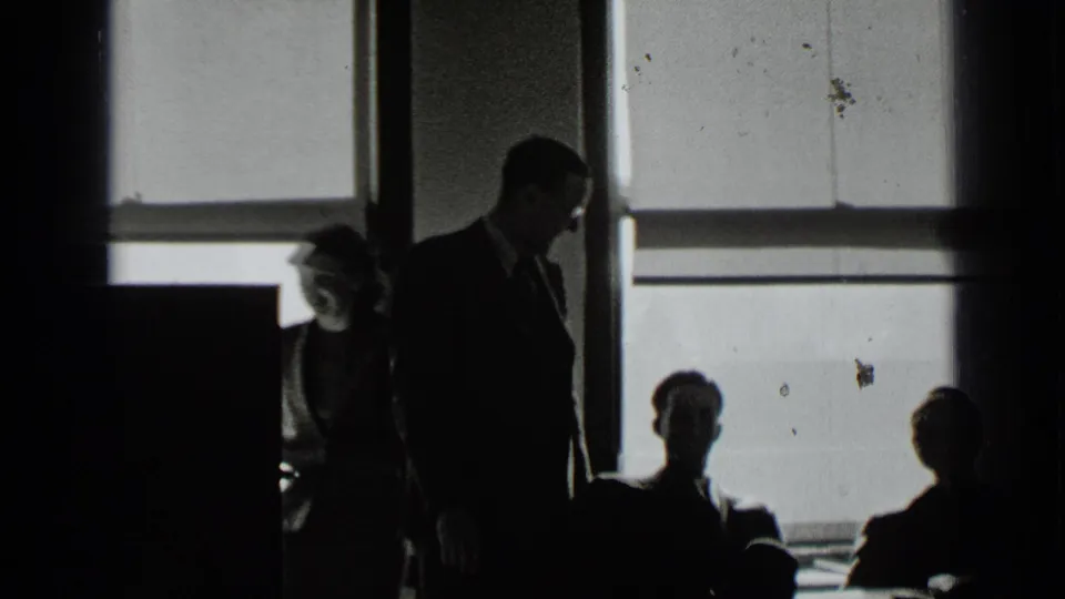1939 New York office interior with silhouetted adults near large windows and a suited man standing beside seated figures.