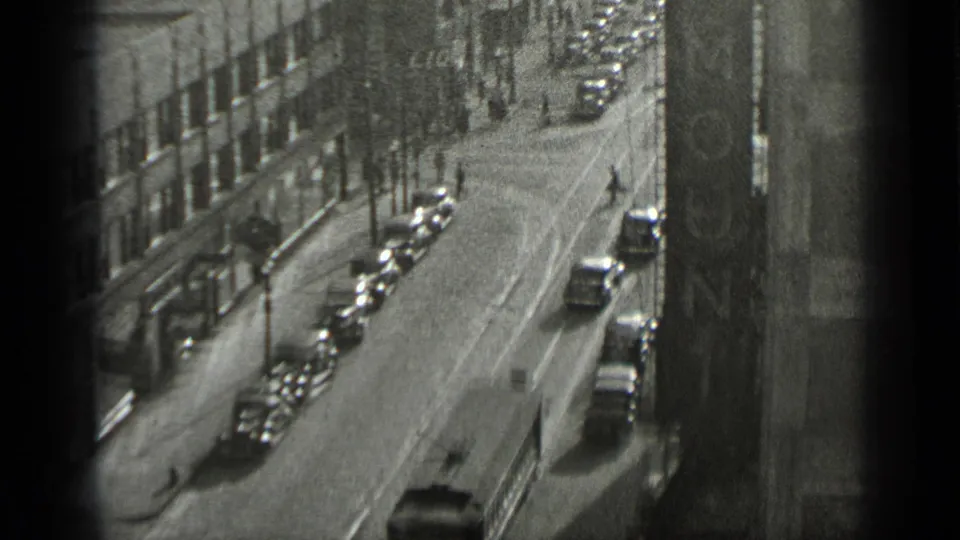 1939 New York street view showing parked vintage cars, sidewalks, pedestrians, and a vertical building sign or facade detail.