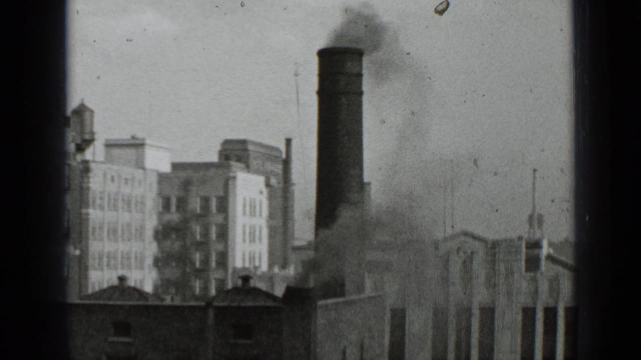 1939 New York 8mm frame showing a tall smokestack releasing dark smoke over brick and masonry city buildings.