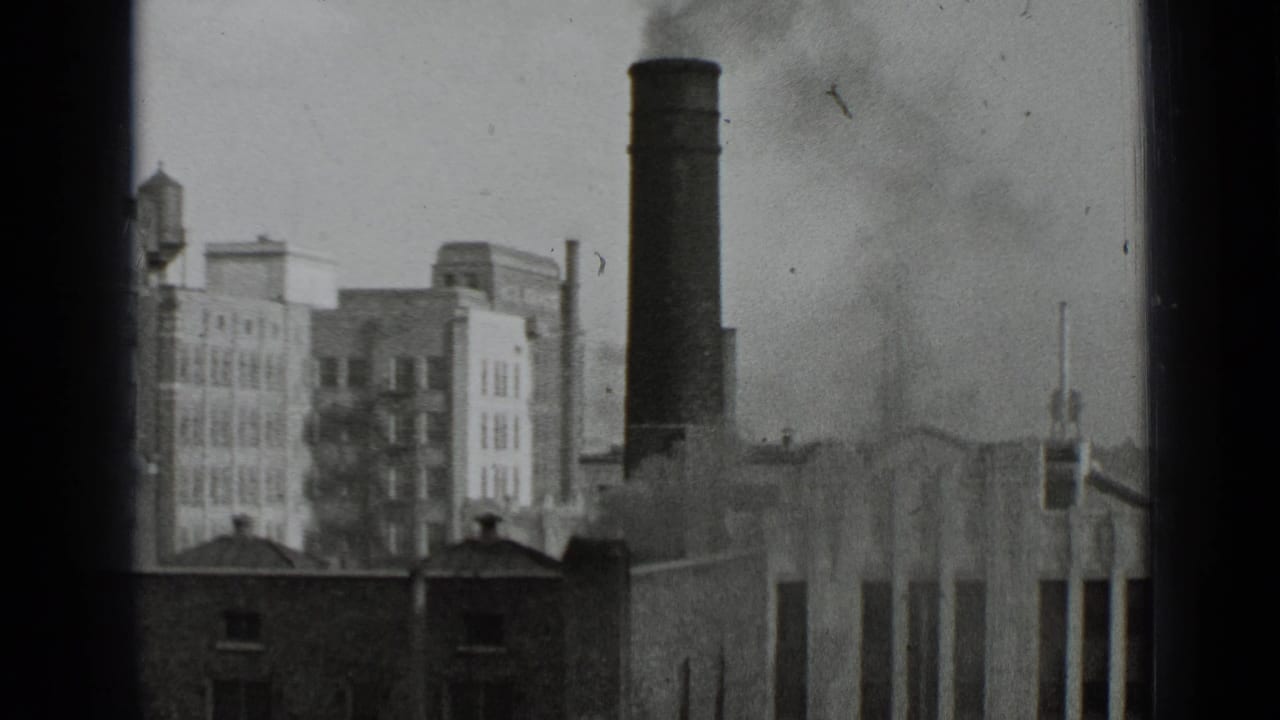 Tall smokestack and city buildings viewed through dark film edges.