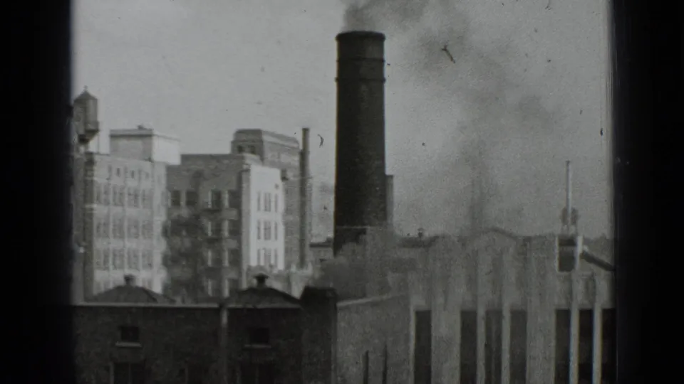 1939 New York city view with a factory smokestack, drifting smoke, surrounding buildings, and visible 8mm frame-edge shadows.