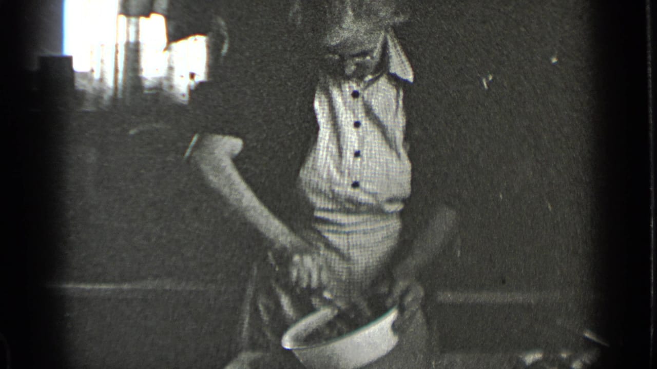 In 1939 New York home-movie footage, a woman in a light apron works over a white bowl in a dim interior.