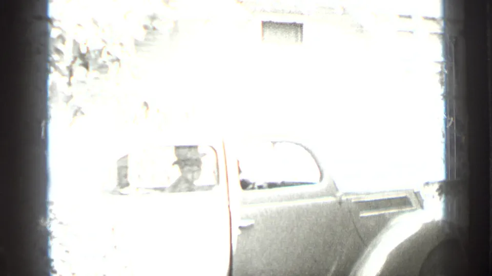 Bright exterior frame from the same New York home movie shows a rounded 1930s car parked beside a residential building.