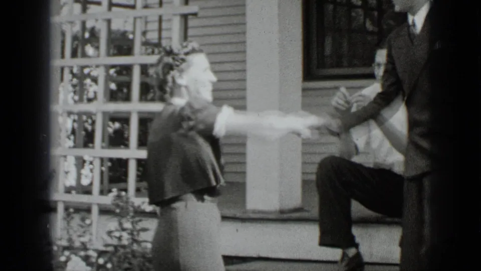 A woman in a dress and hat smiles while extending her hand to a suited man outside a New York house in the supplied 1939 home movie.