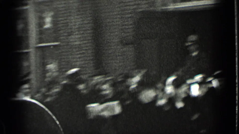 A handheld 8mm frame catches blurred pedestrians and parked cars along a brick-lined New York sidewalk in the 1939 winter scene.