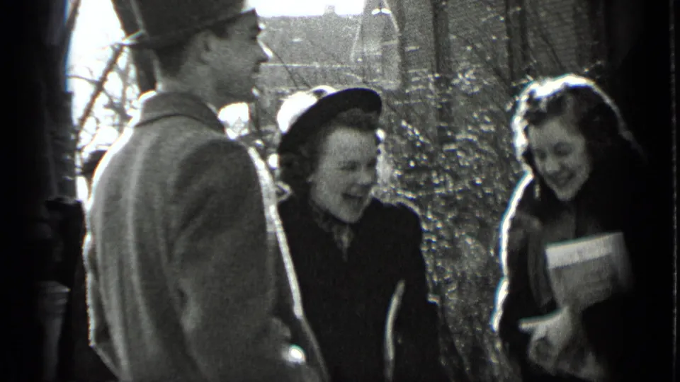 A man in a brimmed hat stands near two smiling women in coats during a 1939 New York sidewalk exchange.