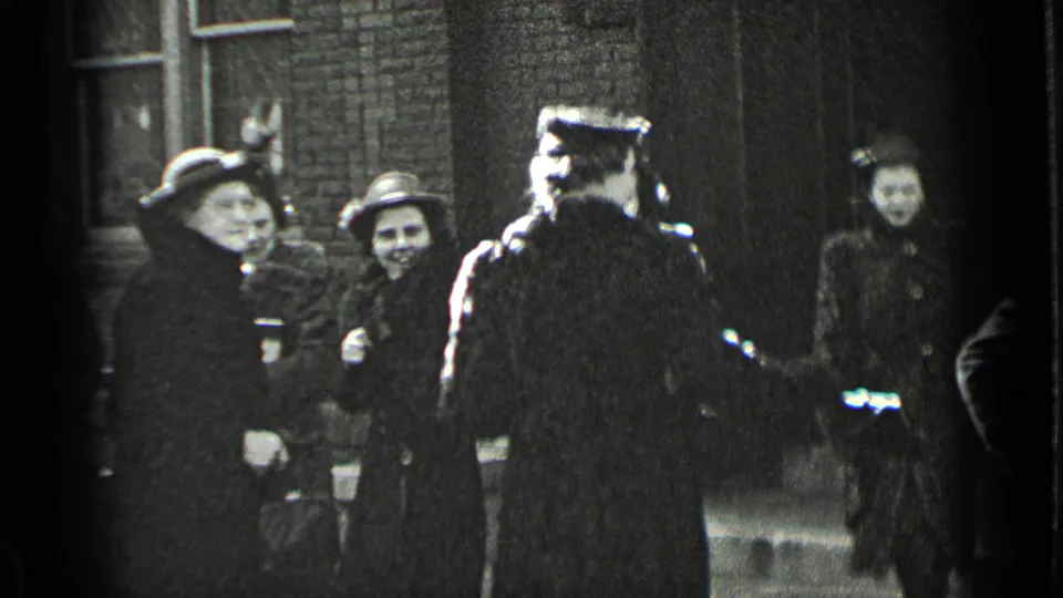 Several adults in winter coats and hats gather near brick buildings in a candid 1939 New York street scene.
