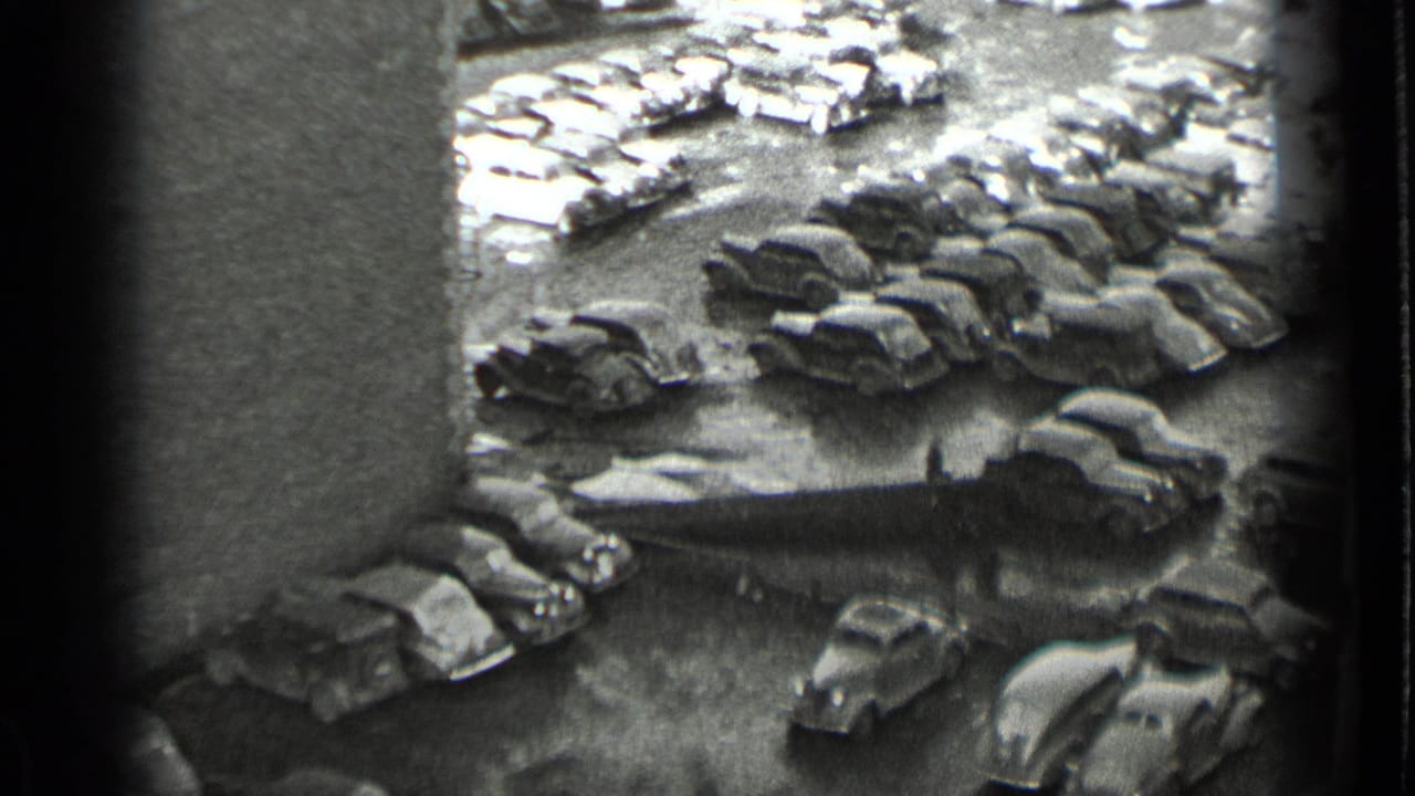 Black-and-white 1939 New York home-movie frame looking down over a crowded lot of late-1930s automobiles.