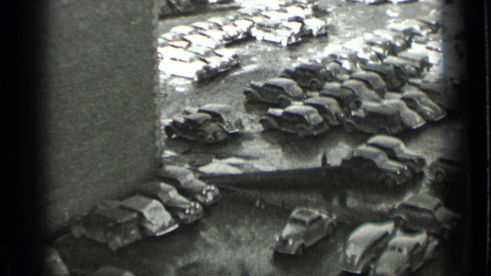 Black-and-white 1939 New York home-movie frame looking down over a crowded lot of late-1930s automobiles.