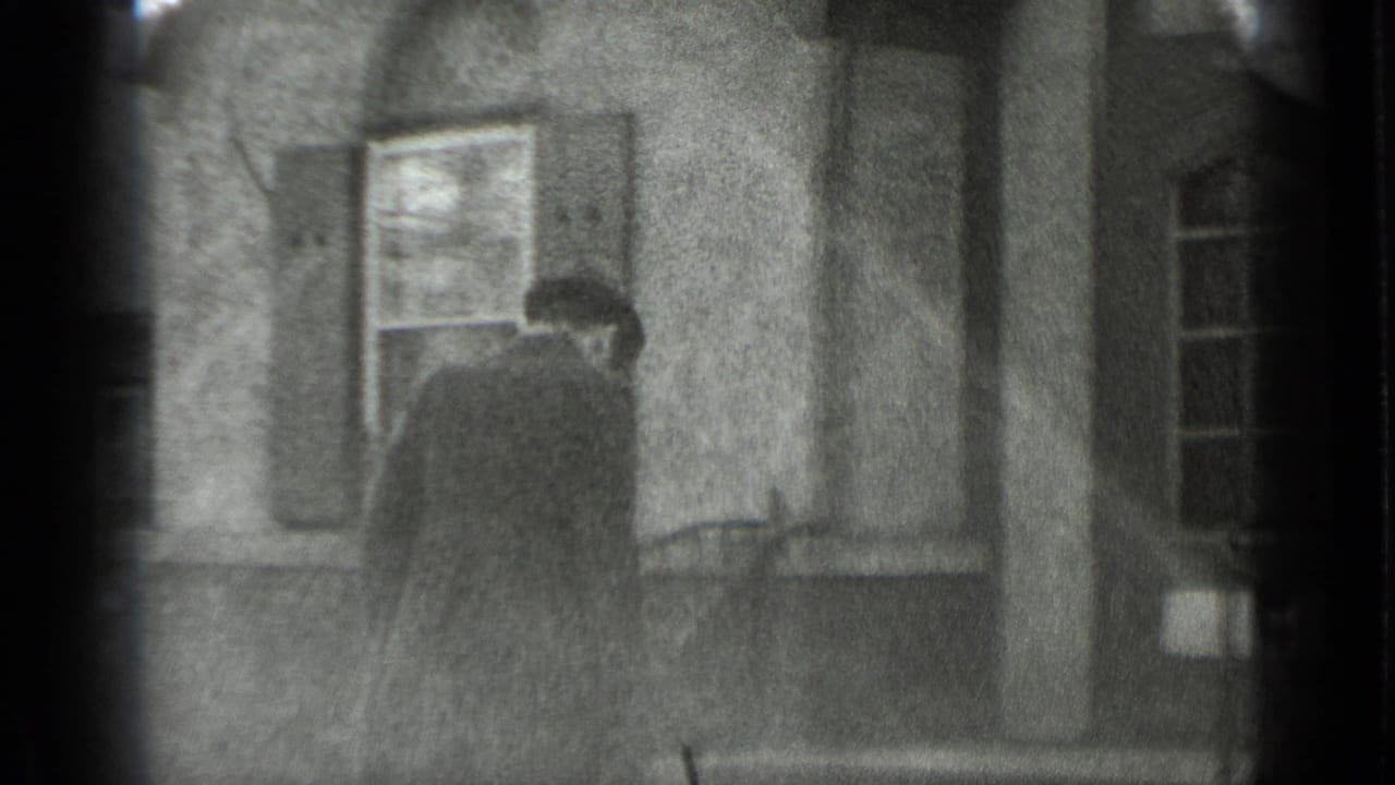 Man in a dark coat and hat stands near steps outside a house.