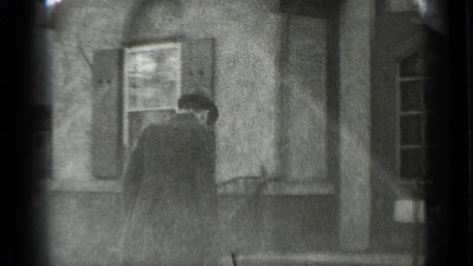 Black-and-white 1939 New York home-movie frame of a man in a dark coat and hat approaching a residential doorway.