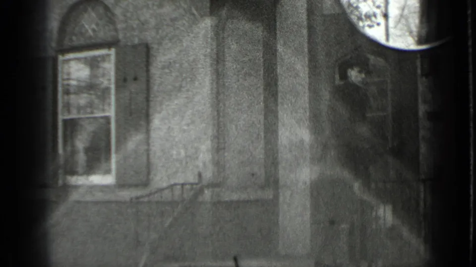 Black-and-white 1939 New York home-movie frame of a man at a house doorway after climbing the exterior stairs.
