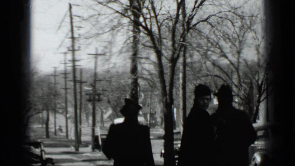A 1939 New York street frame shows dark-coated figures on a snowy sidewalk, one glancing toward the camera beneath leafless trees and utility lines.