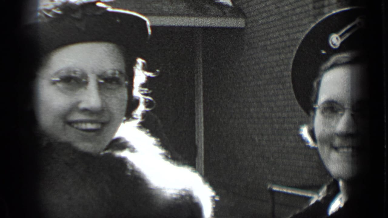 Two smiling adult women in period hats seen in close-up beside a building.
