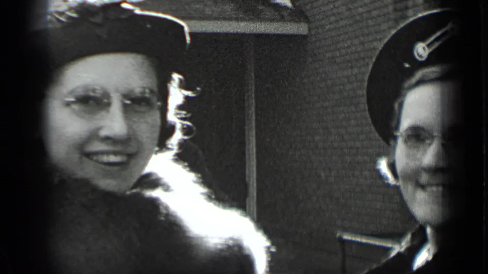 Two adult women in 1930s New York home-movie footage smile toward the camera, one wearing eyeglasses and a fur-trimmed coat.