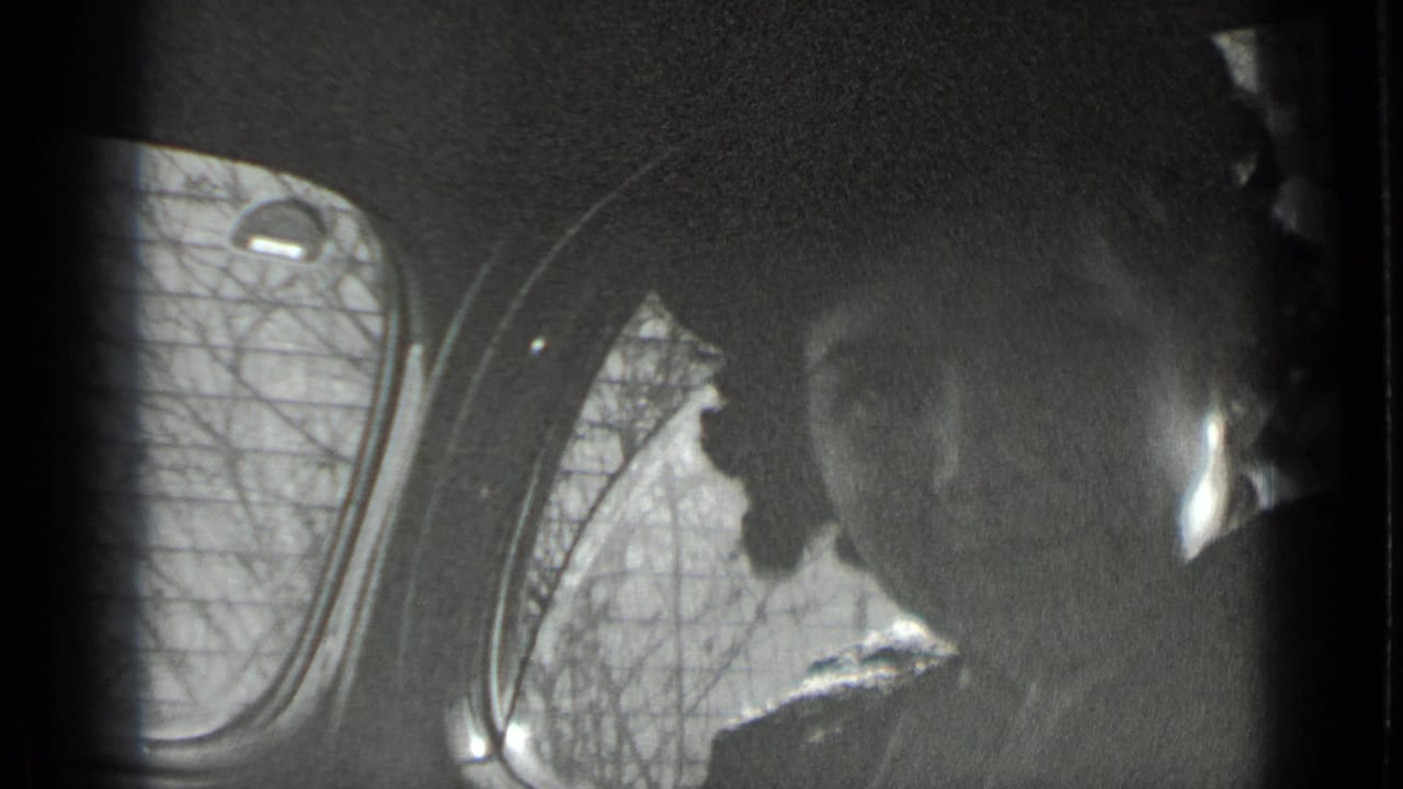 Black-and-white 1939 New York home-movie frame showing shadowed passengers inside a vehicle, with a rounded window and bare trees outside.