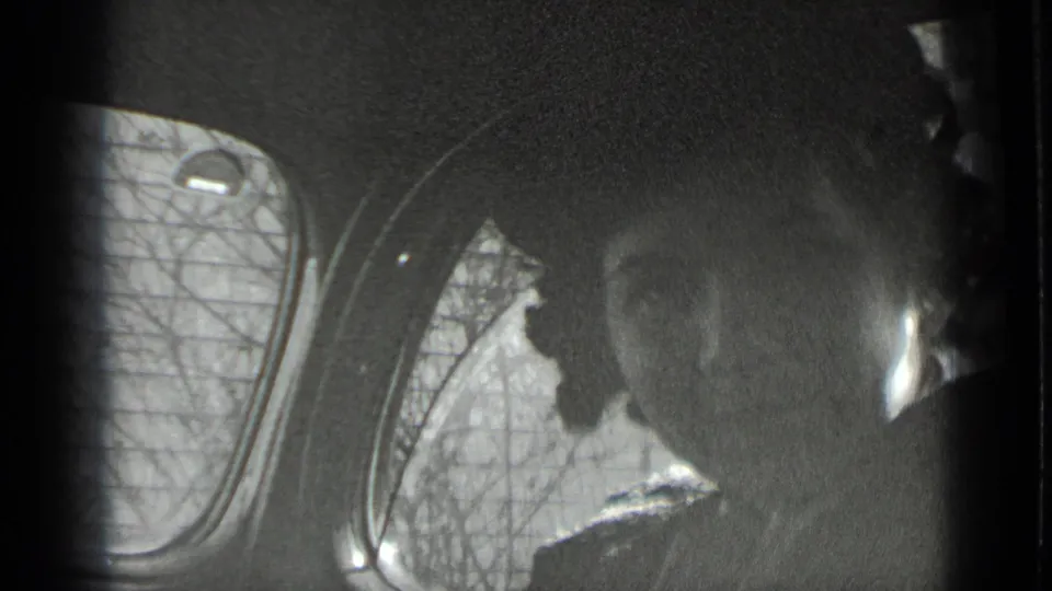 Black-and-white 1939 New York home-movie frame showing shadowed passengers inside a vehicle, with a rounded window and bare trees outside.