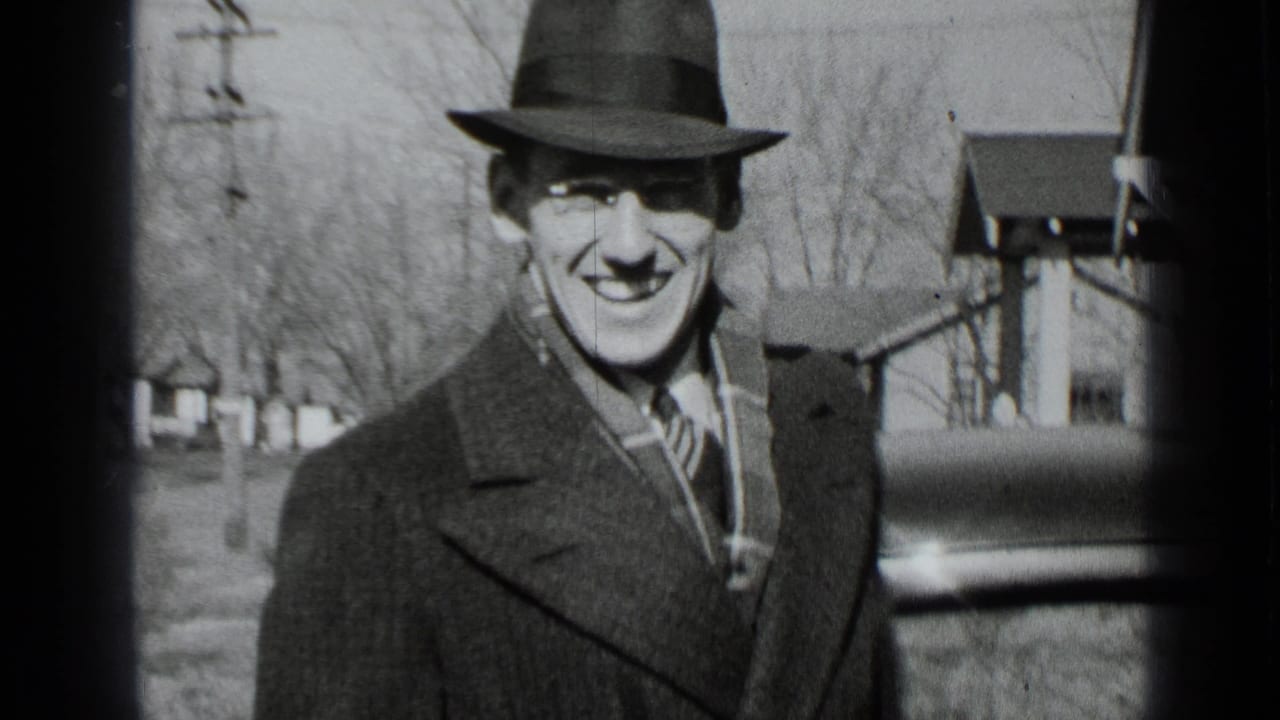 A smiling man in a fedora and overcoat looks toward the camera on a New York residential street in 1939.