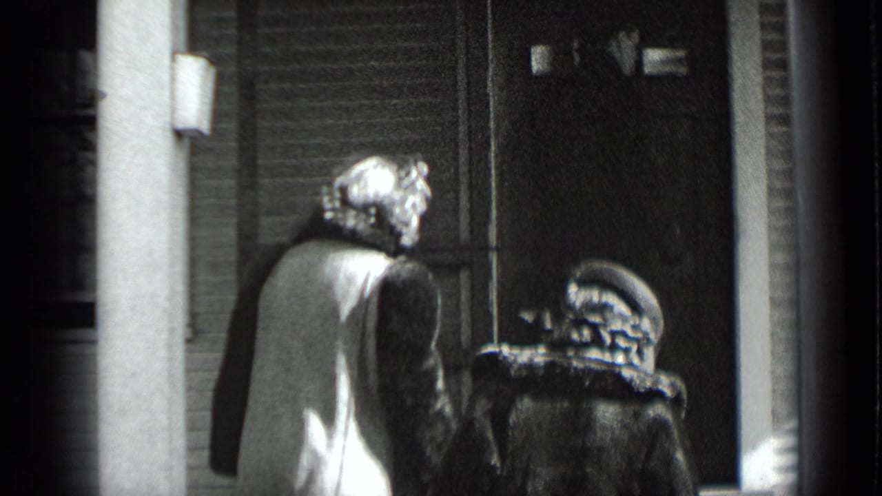 Two women in coats and hats approach a porch doorway beside a column.
