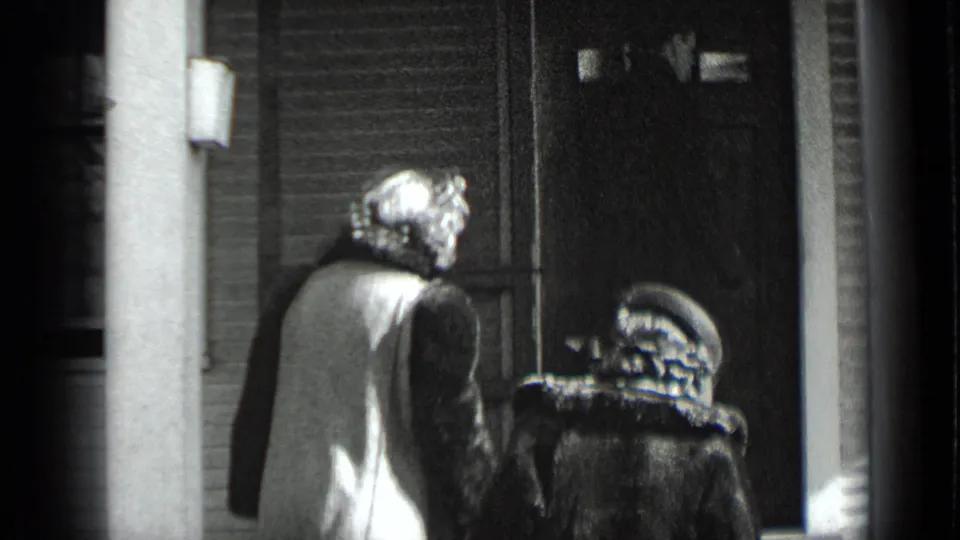 In 1939 New York home-movie footage, two women in winter coats and hats move toward a residential-looking entrance.