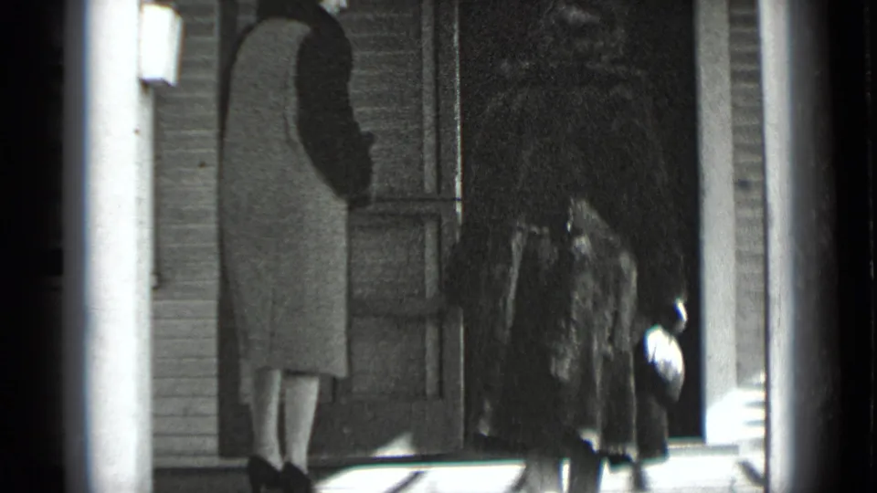 At the doorway, the women pause close together, with the fur-coated woman holding a handbag at her side.