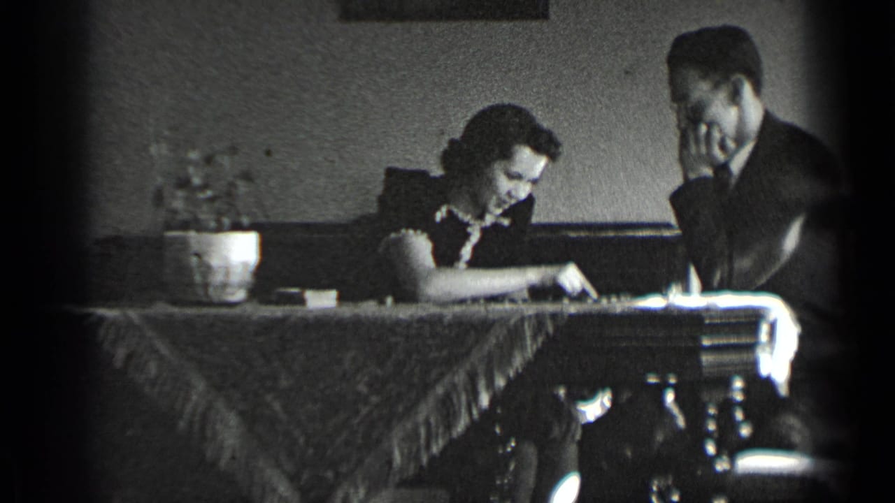 Man and woman sit at a table with a chessboard and potted plant.