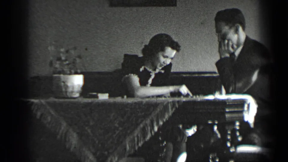 In 1939 New York home-movie footage, a man and woman sit indoors at a fringed table while playing chess.