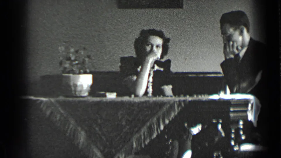 The woman pauses with her hand near her mouth as the man leans beside her during a chess game in a New York interior.