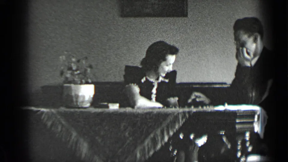 A young couple in a private New York interior studies a checkers board during the brief 1939 home-movie clip.