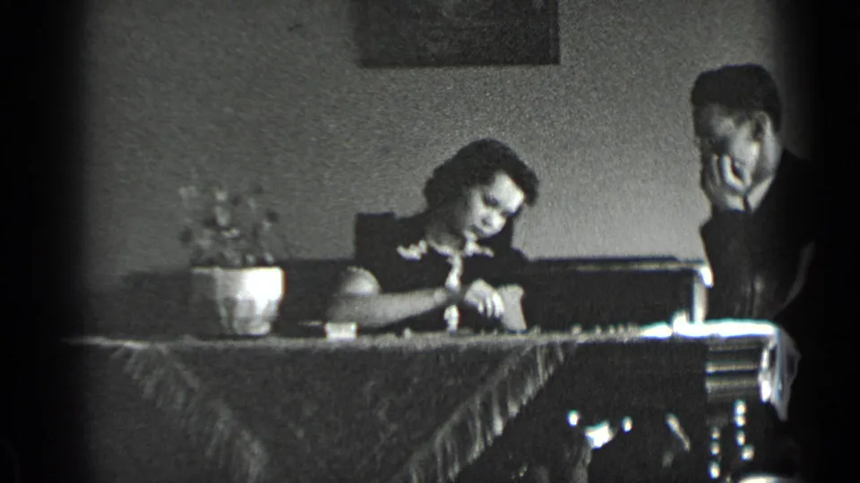 The woman leans over the board and the man watches at the dining table in the 1939 New York home-movie scene.