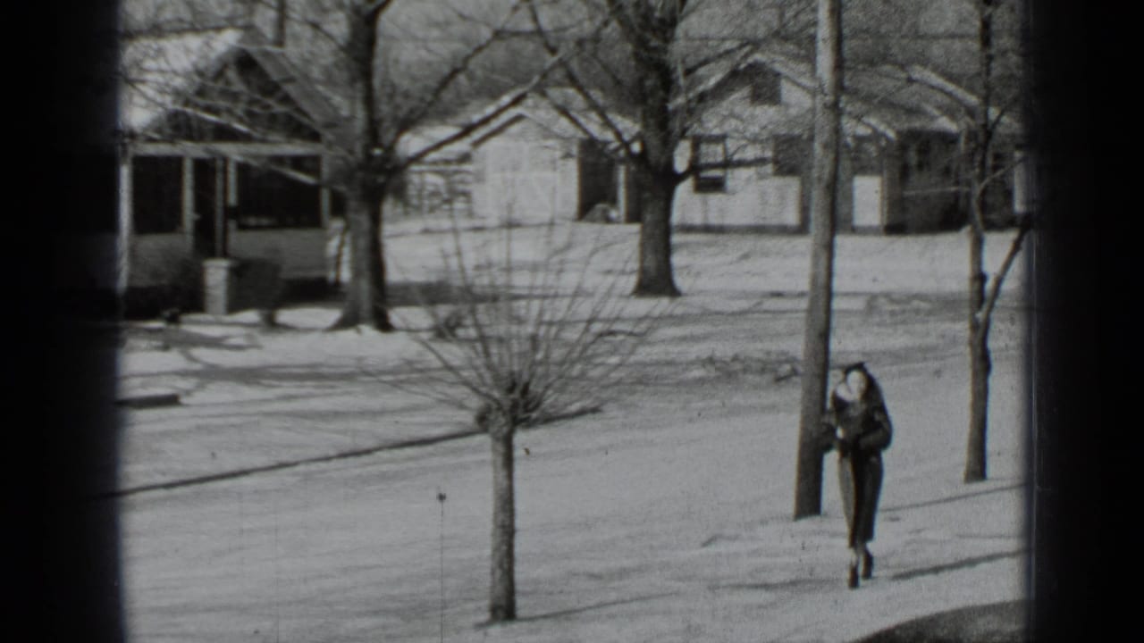 In 1939 New York home-movie footage, a woman in a long coat walks along a snow-dusted residential sidewalk.