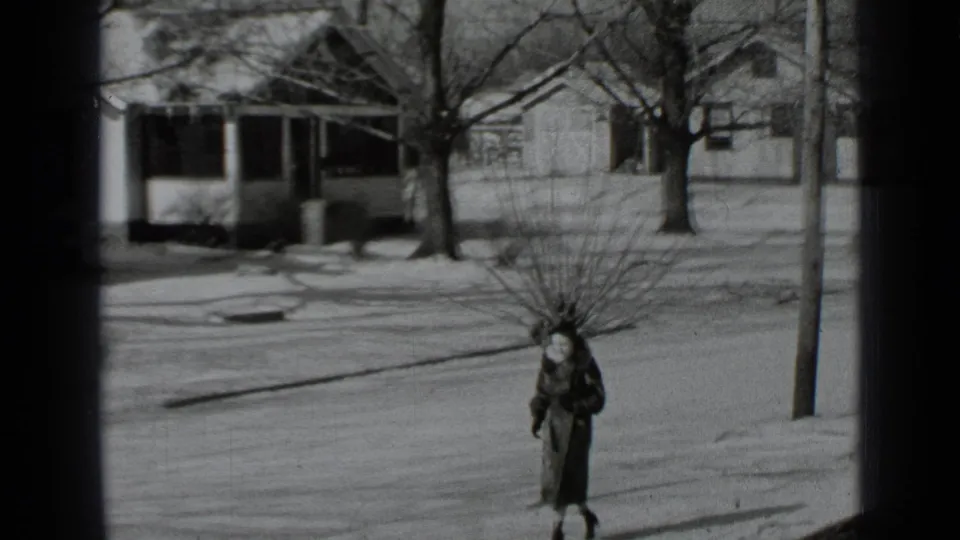A woman in winter clothing approaches on a snow-dusted sidewalk in a 1939 New York residential scene.