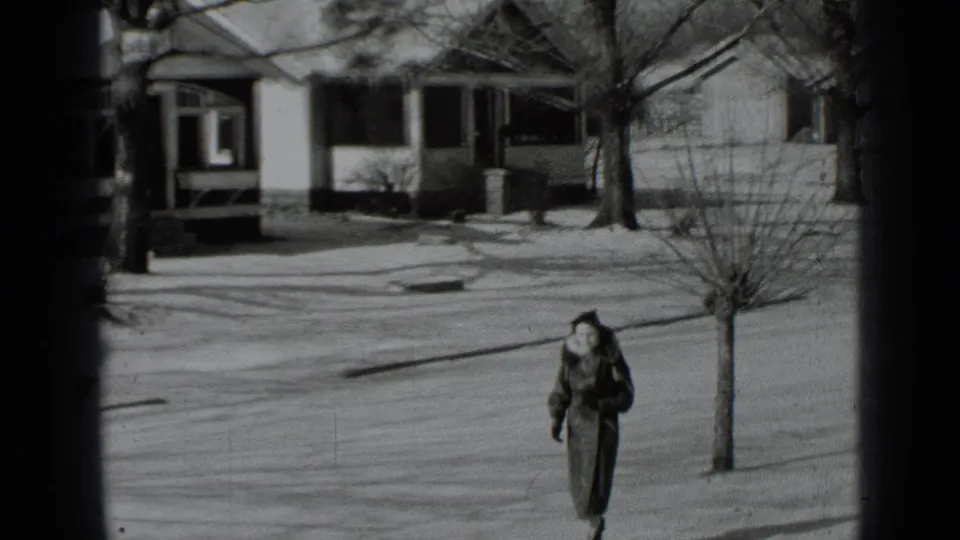 The woman remains on the snowy sidewalk as houses and bare trees frame the 1939 New York home-movie view.